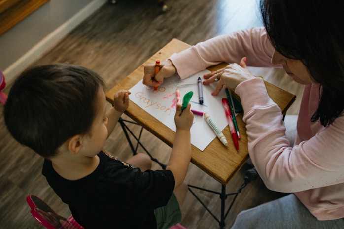 A mother helping her son write his name with markers