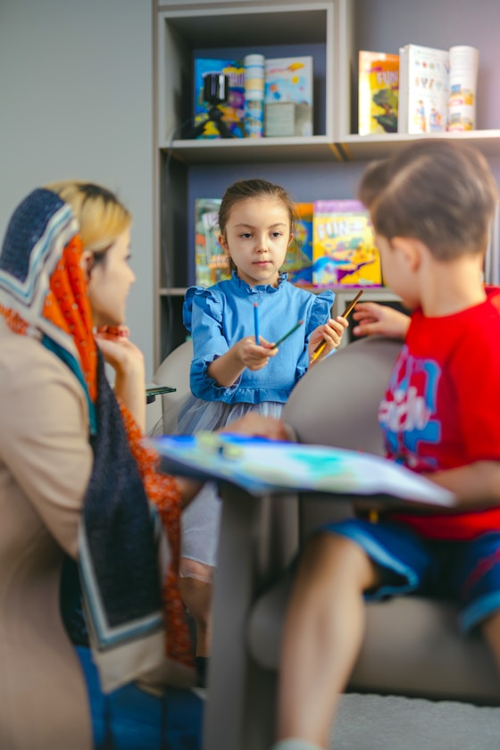 A girl and boy sharing crayons at a table with an adult