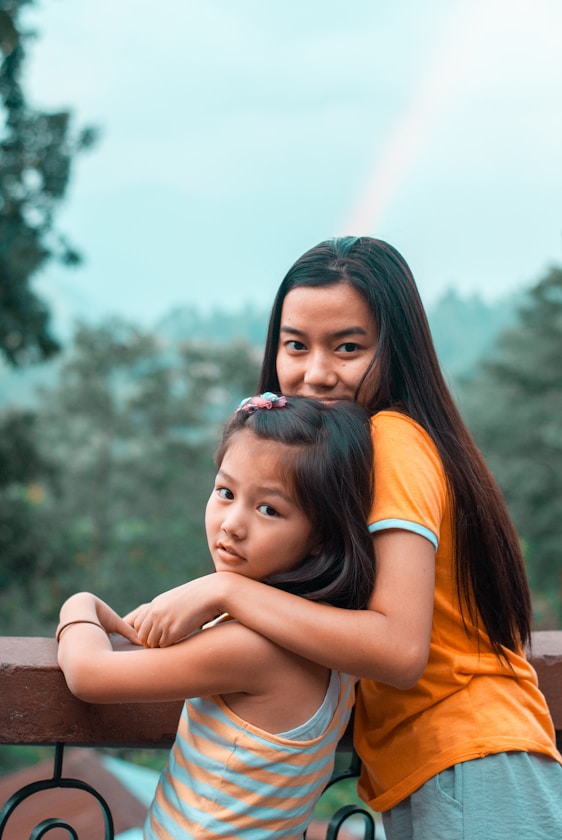 An older sister embracing her younger sister outdoors