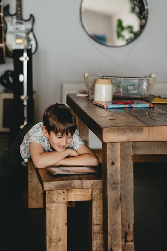A boy resting on a wooden bench looking at a tablet