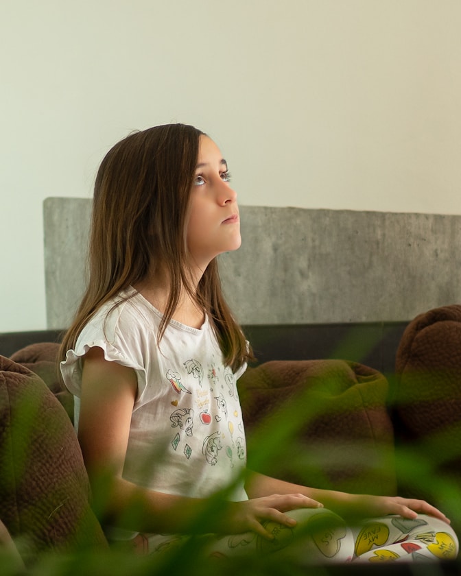 A girl sitting thoughtfully on a sofa, looking upward