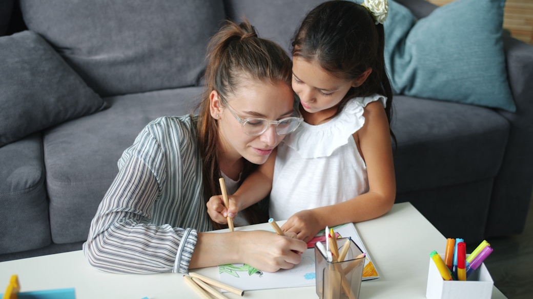 A mother helping her daughter with a drawing on the sofa