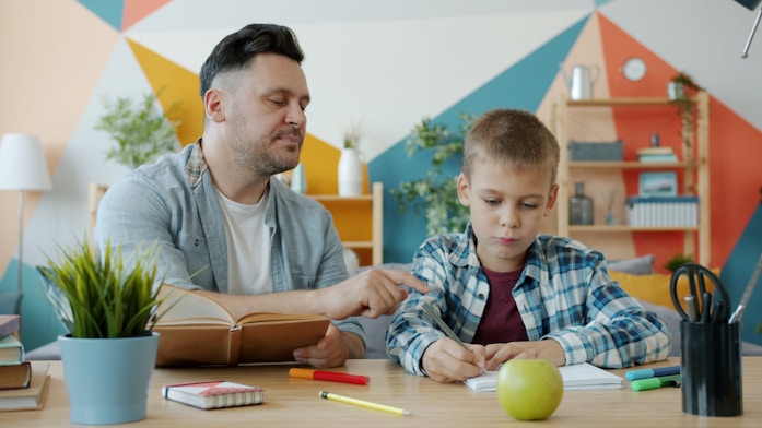 A father helping his son with schoolwork at a colourful desk
