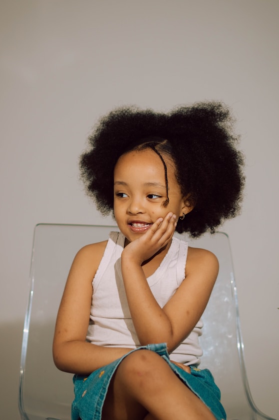 A girl smiling while seated on a clear chair