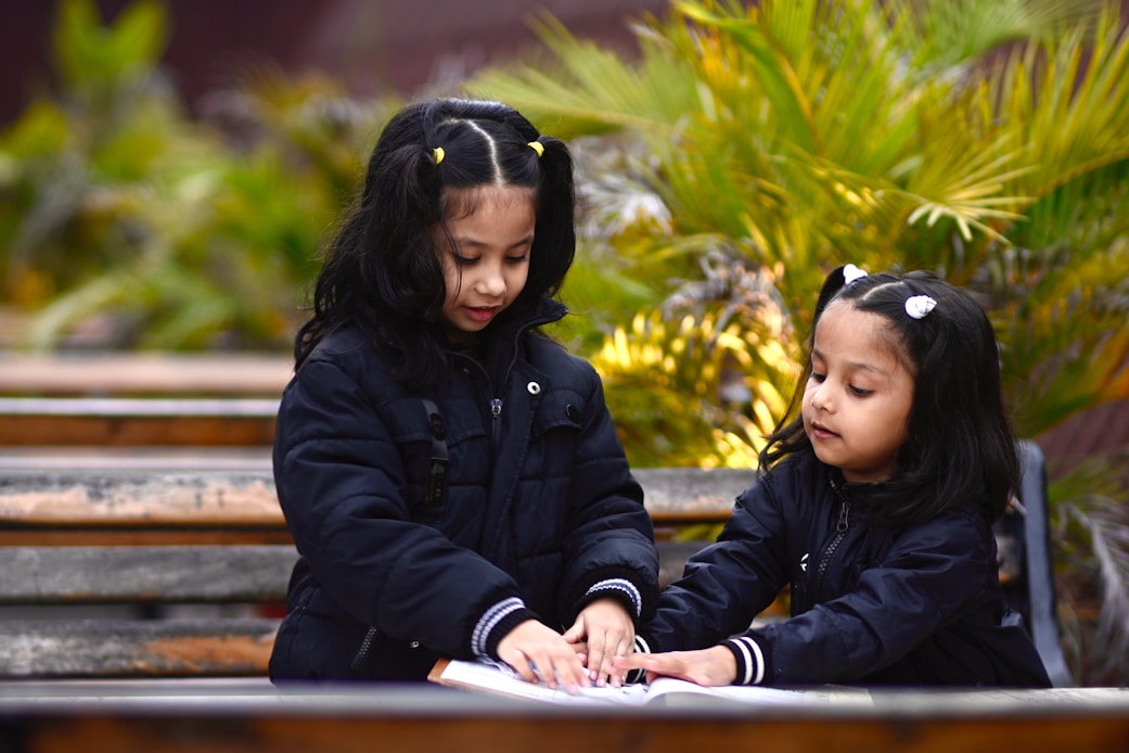 Two girls sitting together outdoors near palm plants