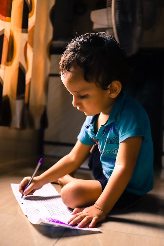 A boy writing in a notebook while sitting on the floor