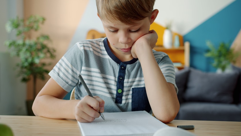 A boy resting his head on his hand while writing at a table