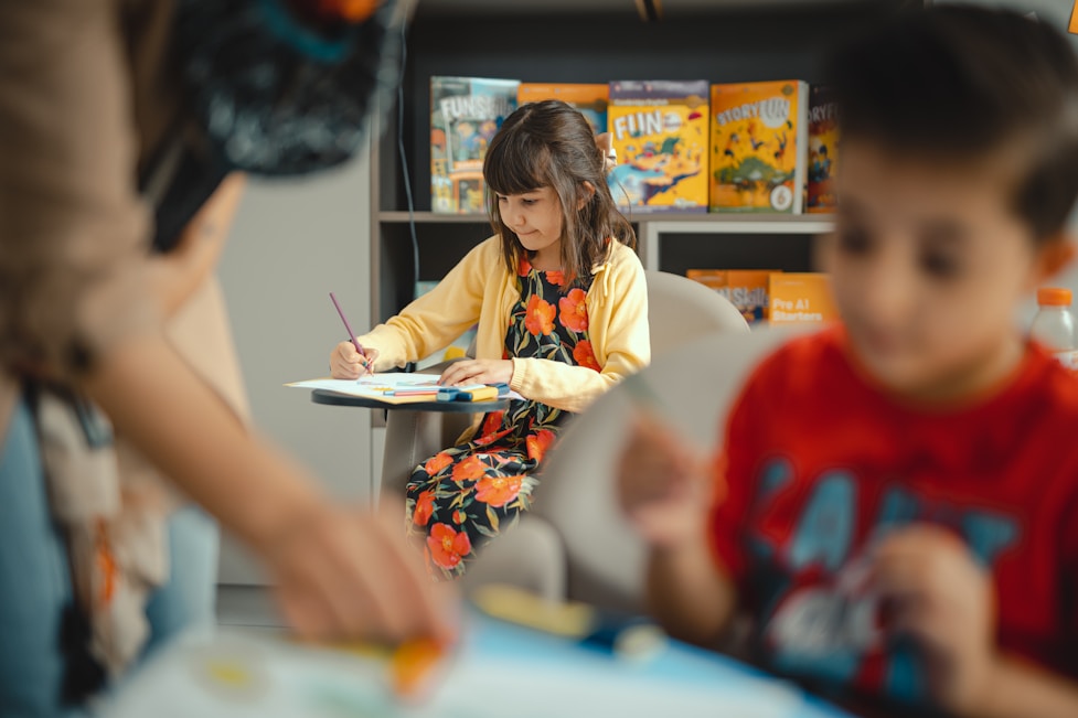 A girl drawing at a table in a room with a bookshelf
