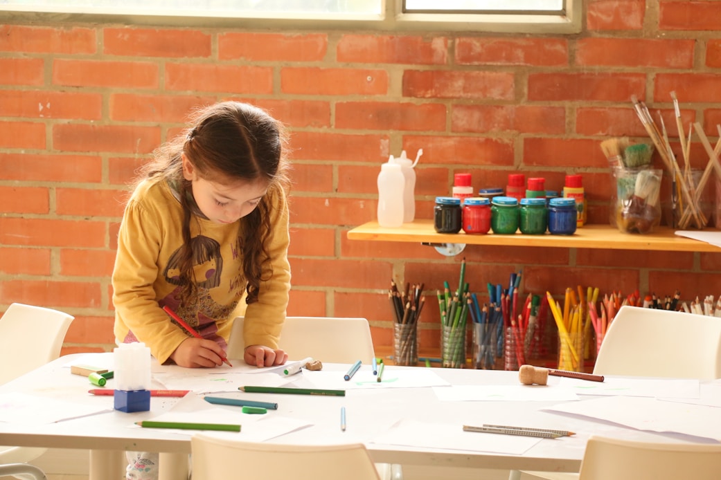 A girl painting at a table against a brick wall
