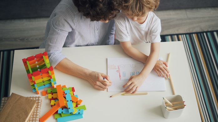 A mother and son drawing together at a table with colourful blocks