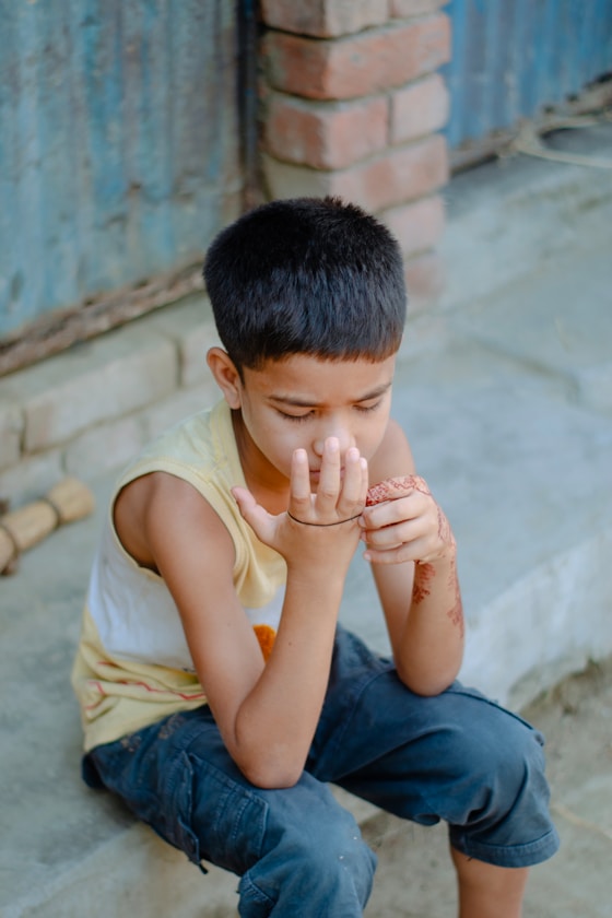 A boy sitting on a step with his hand near his mouth