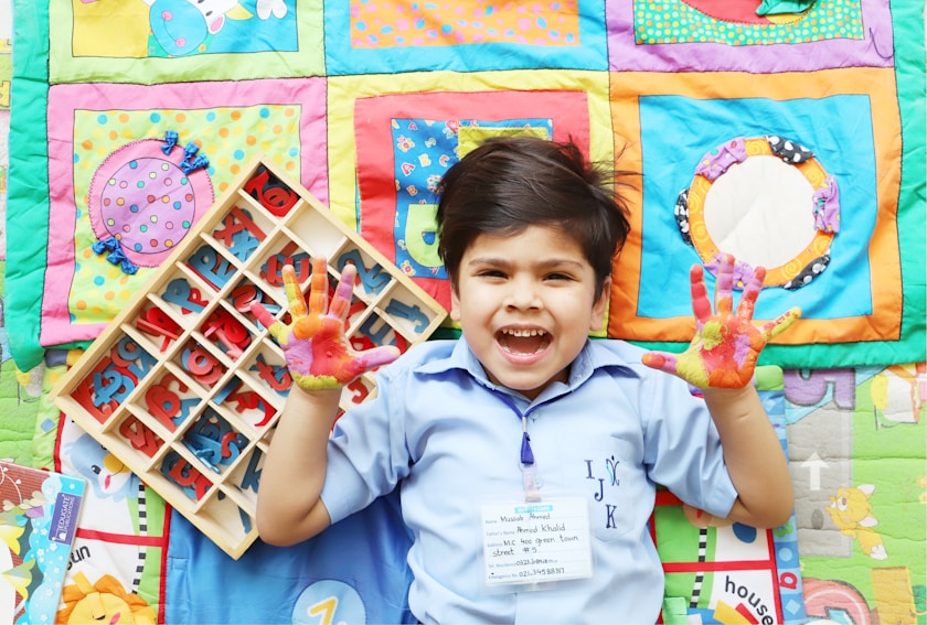 A boy with painted hands lying on a colourful play mat