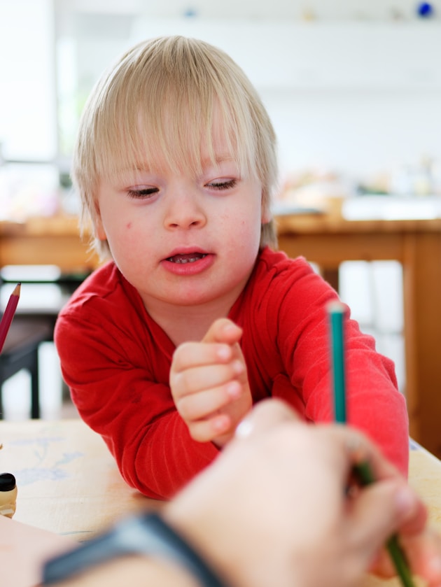 A boy reaching for a pencil at a table