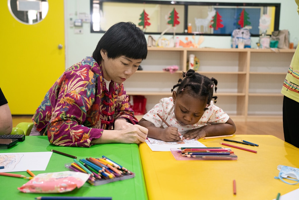 A woman helping a young girl with a colouring activity