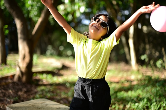 A child wearing sunglasses with arms raised outdoors