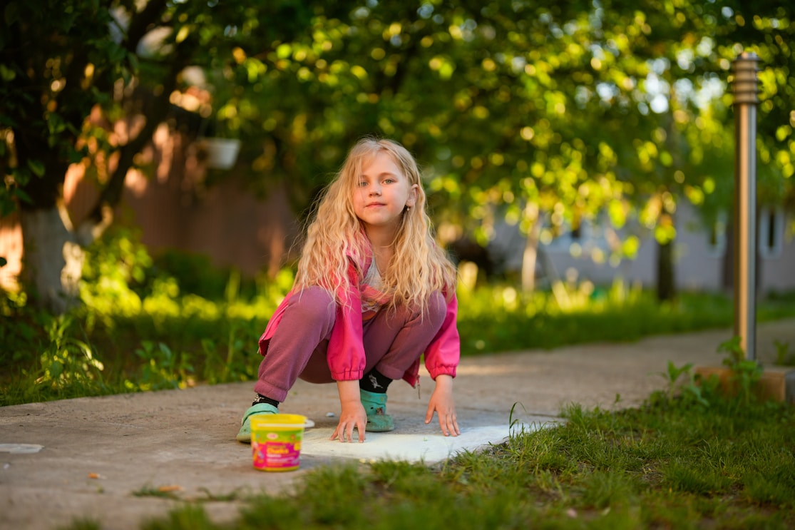 A girl crouching to draw with chalk on a path outdoors