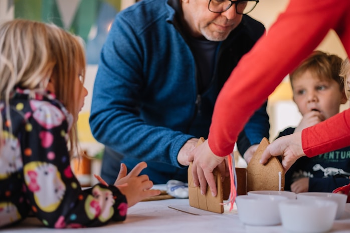 A grandfather helping children build a gingerbread house