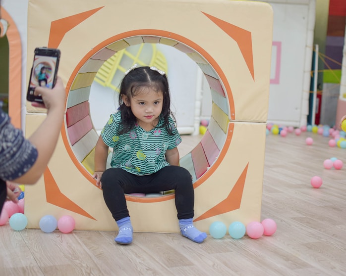 A girl sitting inside a play tunnel surrounded by balls