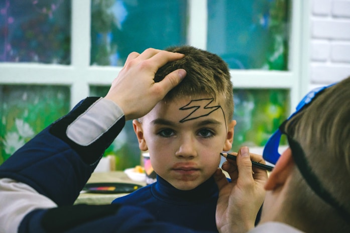 A boy having his face painted with a lightning bolt design