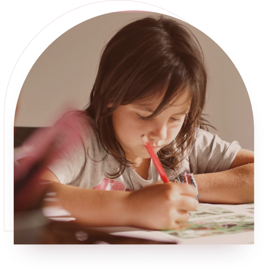 A girl concentrating while drawing with a red pencil at a desk