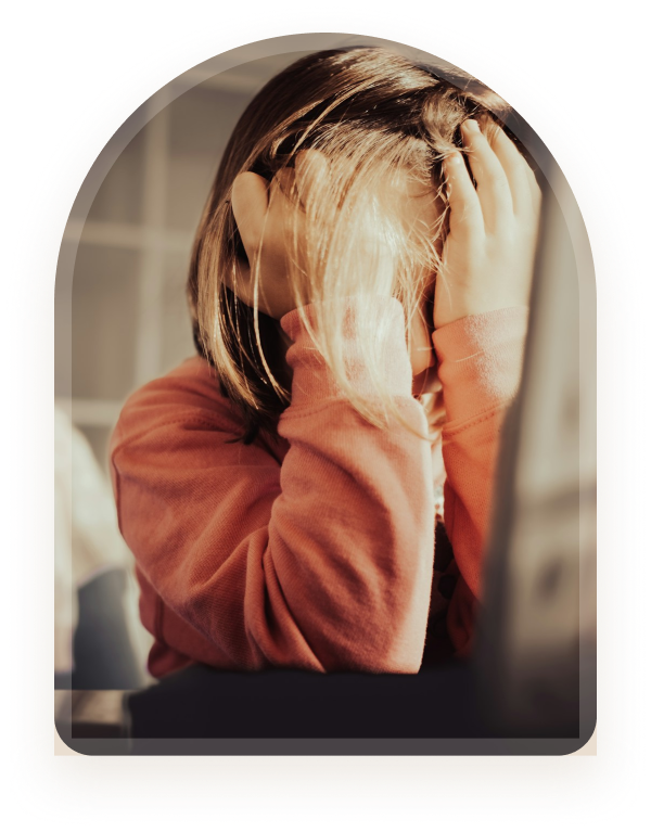 A young person sitting with their head down, hands resting in their hair