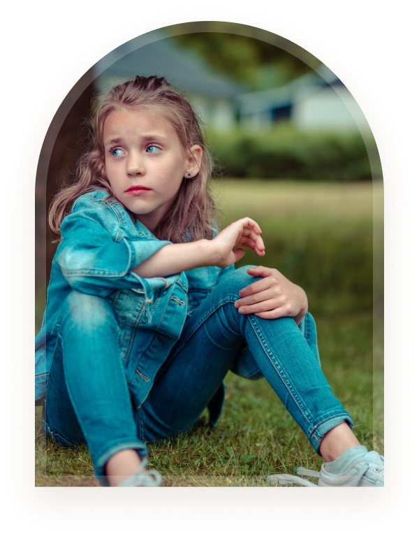 A girl sitting outdoors on grass looking thoughtful