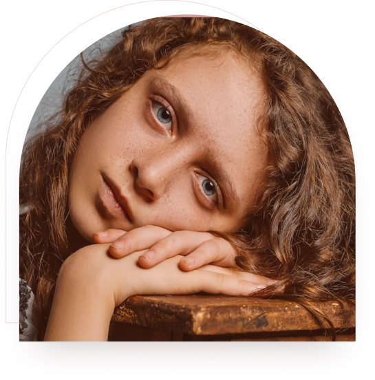 A young person resting their head on their arms on a wooden table