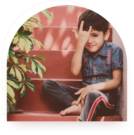 A boy sitting on steps outdoors near green plants