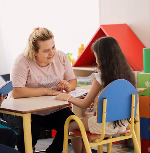 A Hiba specialist working with a child at a desk in a bright classroom setting